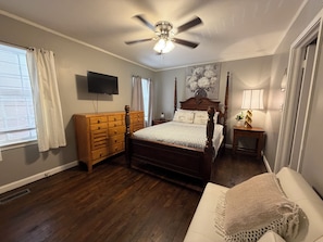 Un dormitorio con cama con dosel, cómoda de madera, ventilador de techo y televisor en la pared.