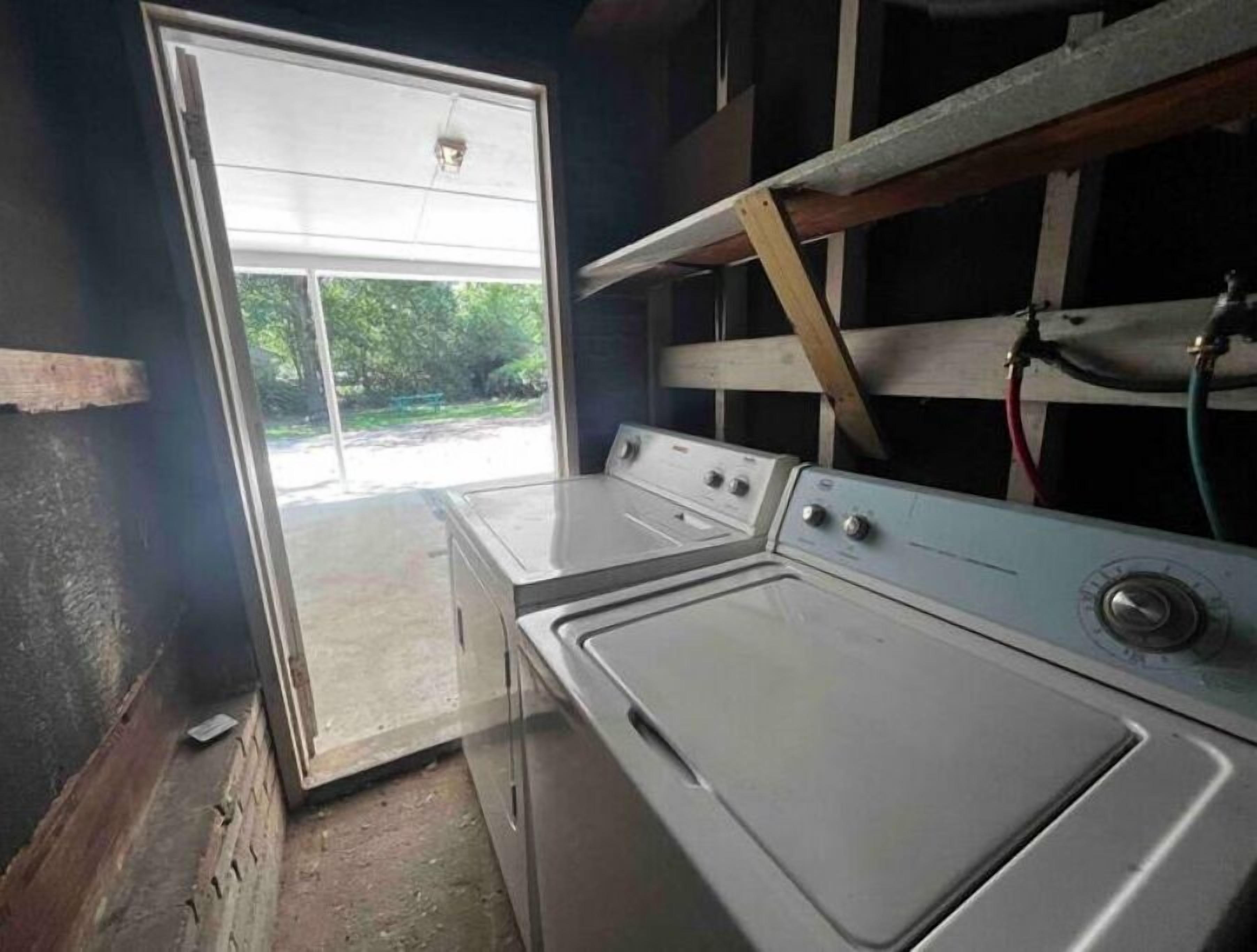 A laundry room with two washing machines, a wooden beam, and a door leading outside.