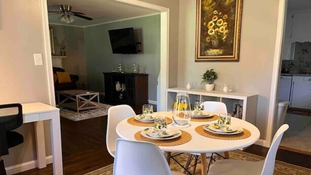 A dining area with a round table set for four, surrounded by white chairs. There is a painting of flowers on the wall above the table. - Spacious 3BR House • Sleeps 8 • Near SGMC, VSU & Moody AFB • Parking (Valdosta)