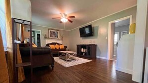 A living room with a dark wood floor, a brown leather sofa, a white coffee table, a dark wooden cabinet, and a ceiling fan. - Spacious 3BR House • Sleeps 8 • Near SGMC, VSU & Moody AFB • Parking (Valdosta)