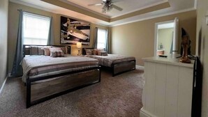 Ein Schlafzimmer mit zwei Betten, einem Deckenventilator, einem großen abstrakten Gemälde und einer Kommode.
