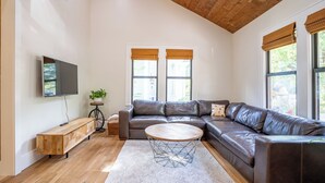 Ein modernes Wohnzimmer mit einem ledernen Ecksofa, einem runden Couchtisch und einem an der Wand befestigten Fernseher.