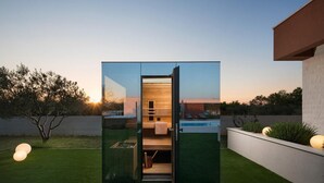 A modern outdoor sauna with a wooden interior, a glass door, and a view of a pool and garden at dusk. - Lovely home in Benkovac with sauna (Benkovac)
