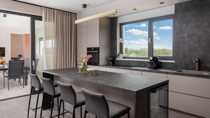 A modern kitchen with a large island, bar stools, a coffee machine, and a window with a view. - Lovely home in Benkovac with sauna (Benkovac)