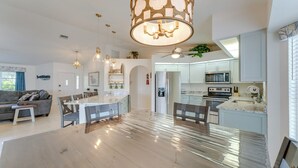 Een ruime woonkamer met een grote houten eettafel, een keuken met moderne apparatuur, en een plafondventilator.