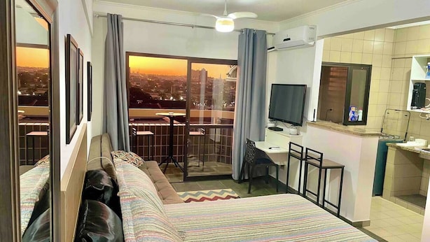 A hotel room with a bed, a desk, a chair, a TV, and a balcony with a city view.