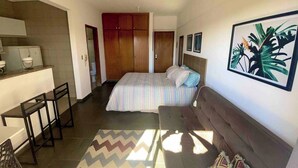 A compact hotel room with a bed, a sofa, a small kitchenette, and a bathroom.