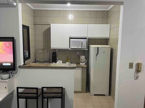 Uma cozinha compacta com micro-ondas, geladeira e cafeteira no balcão.