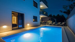A modern outdoor pool area with a clear blue pool, a covered seating area, and a two-story building with balconies. - Beautiful home in Vir (Vir)
