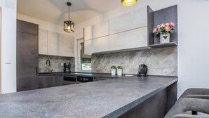 A modern kitchen with a large island, dark cabinets, and a built-in oven. There are two potted plants on the island and a coffee maker on the counter. - Beautiful home in Vir (Vir)