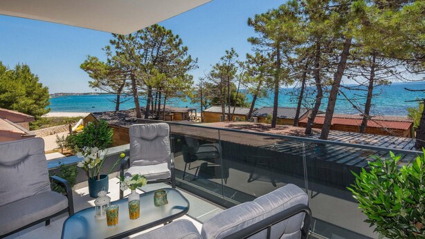 A balcony with a glass table, two grey sofas, and a view of the sea and pine trees. - Beautiful home in Vir (Vir)