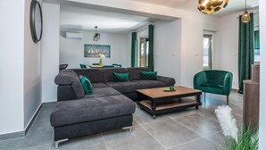 A modern living room with a sectional sofa, a coffee table, and a green armchair. There is a dining area in the background with a table and chairs. - Beautiful home in Vir (Vir)