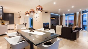 A modern living room with a glass dining table, white chairs, a black sofa, and a fireplace. - Luxurious home in Gradina (Gradina)