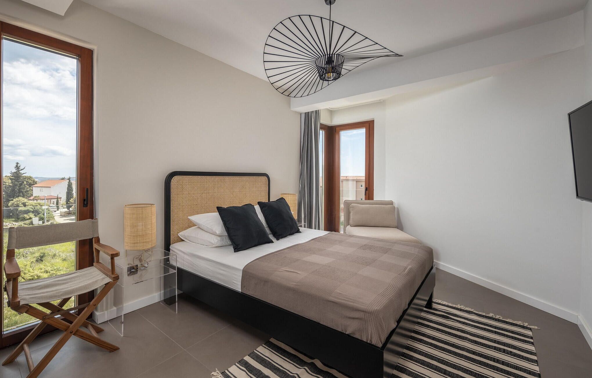 Une chambre à coucher moderne avec un lit, une chaise, une lampe et une vue sur l’extérieur.