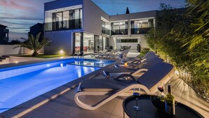 Una casa moderna de dos pisos con piscina, sillas de descanso y comedor.