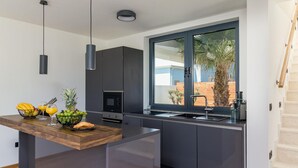 Una cocina moderna con una isla de madera, armarios oscuros y un amplio ventanal con vistas a palmeras.