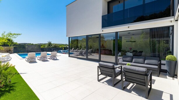 Una casa moderna con piscina, mobiliario exterior y grandes ventanales.