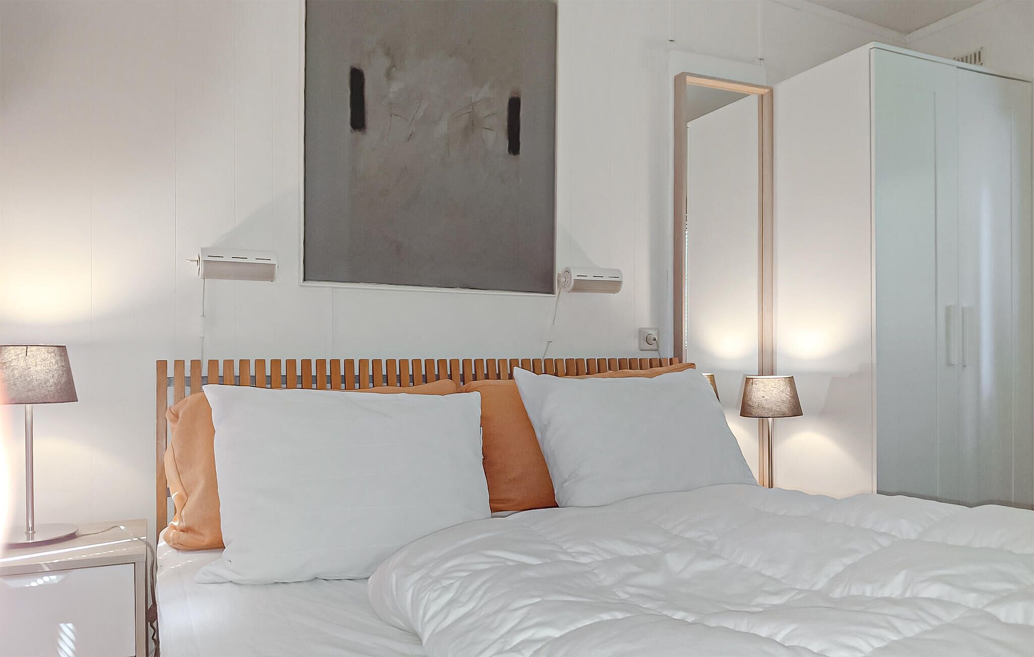 Un dormitorio con cama, dos lámparas de noche, un radiador, un armario y un cuadro en la pared.