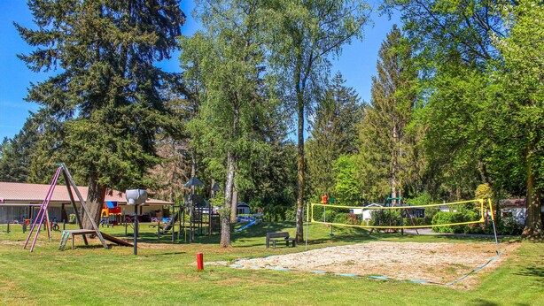 Un terrain de jeux doté de diverses structures ludiques, d’un bac à sable et entouré d’arbres.
