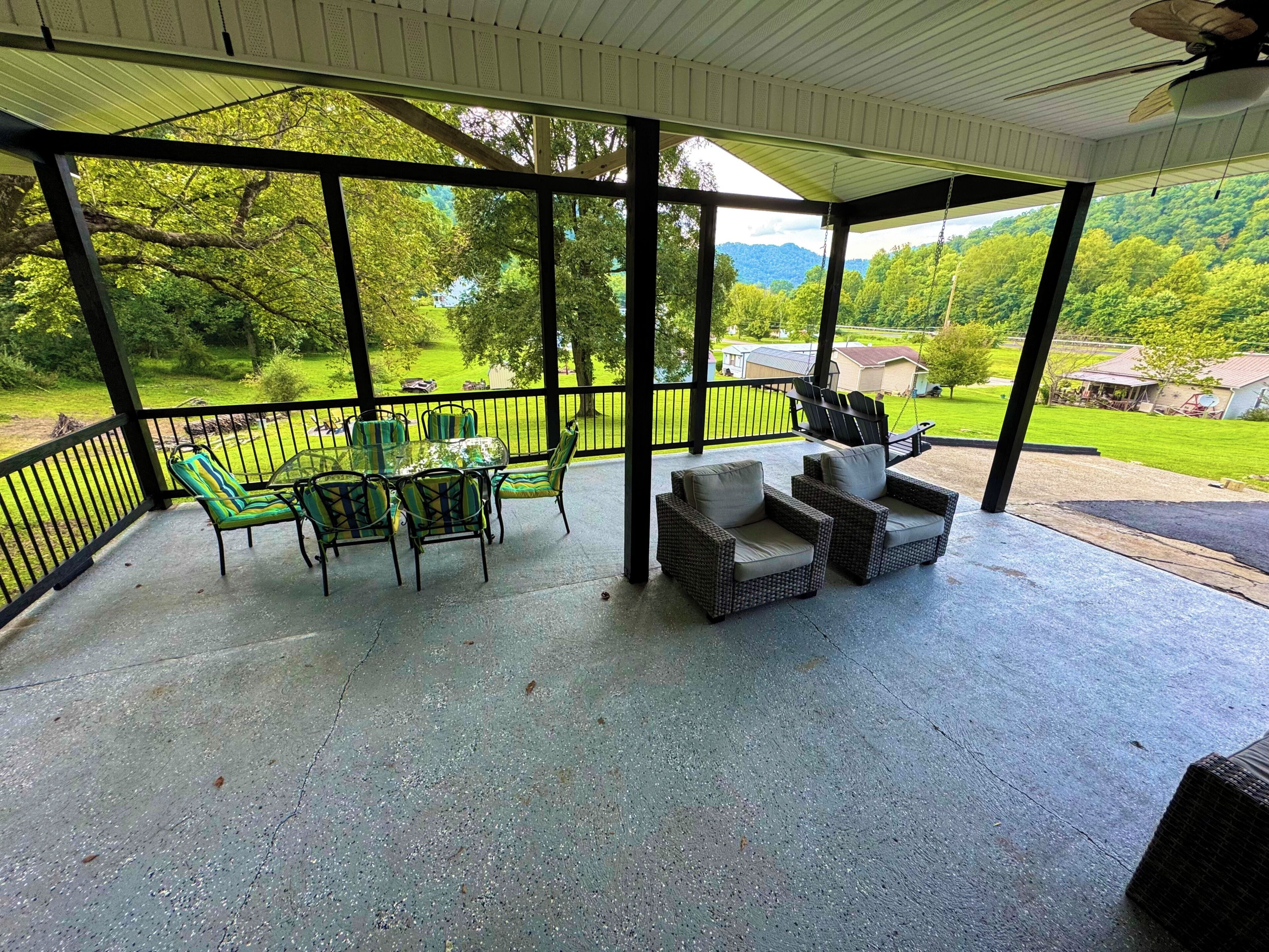 Un patio techado al aire libre con una mesa, sillas, una hamaca y vistas a un paisaje verde.