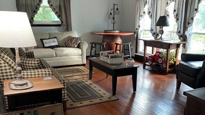 A cozy living room with a sofa, coffee table, and a fireplace. There is a wooden coffee table with a sign that reads "Rocky Trails." The room has hardwood floors and a ceiling fan. - Beautiful Mountain View’s and Located on several acres for privacy (Chapmanville)