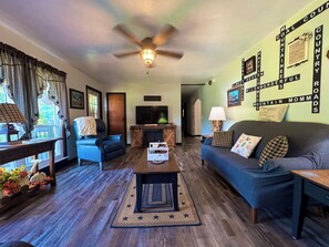 A living room with a fireplace, a ceiling fan, and a wall with a country-themed word search.