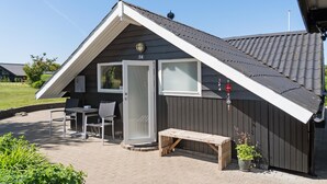 A small, dark-colored building with a sloped roof, a patio with a table and chairs, and a potted plant. - Awesome home in Hejls with WiFi (Hejls)