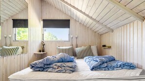 A bedroom with a sloped ceiling, a bed with blue bedding, two bedside tables with lamps, and a window with a view of greenery. - Awesome home in Hejls with WiFi (Hejls)