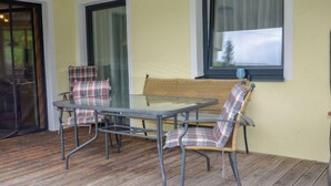 Een terras met een glazen tafel en twee geruite stoelen, een rieten bank en een schuifpui.