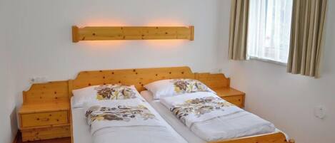A double bed with a wooden headboard, two bedside tables, and a window with curtains.