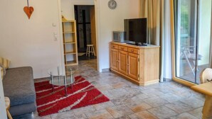 Een woonkamer met een bank, een rood tapijt, een tv op een houten kast en een groot raam met gordijnen.