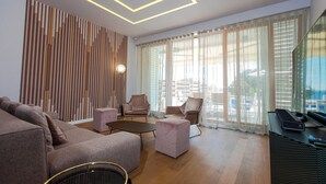Una sala de estar moderna con un sofá, sillas, una mesa de centro y un televisor. Hay un ventanal con cortinas traslúcidas y vistas al exterior.