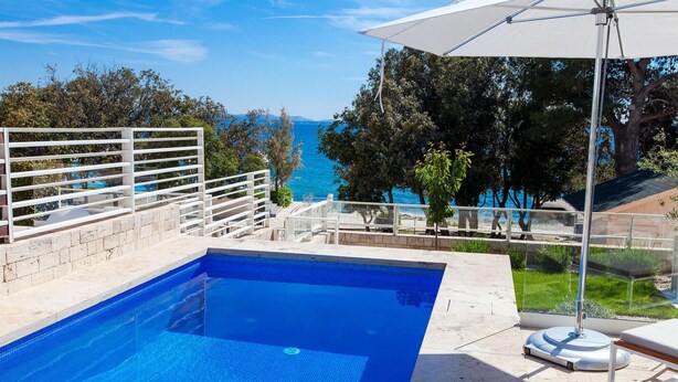 Una piscina con vistas al mar, una sombrilla blanca y una cerca blanca.