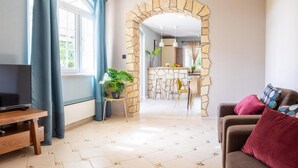 A living room with a stone archway leading to a kitchen, a TV on a wooden stand, and a sofa with cushions. - 4 bedroom beautiful home in Klimno (Klimno)