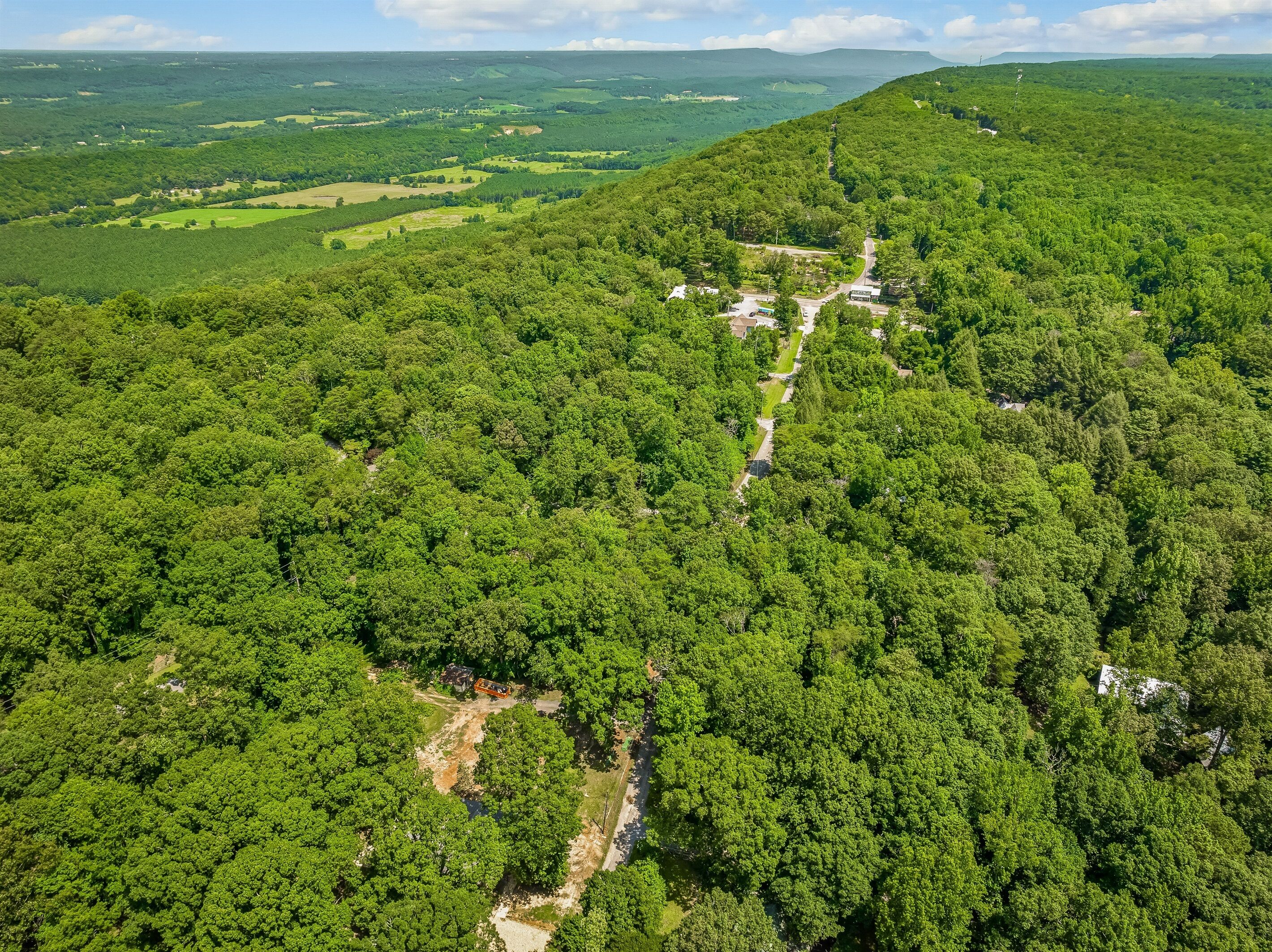 An aerial view of a forested area with a winding path leading to a small cluster of buildings.