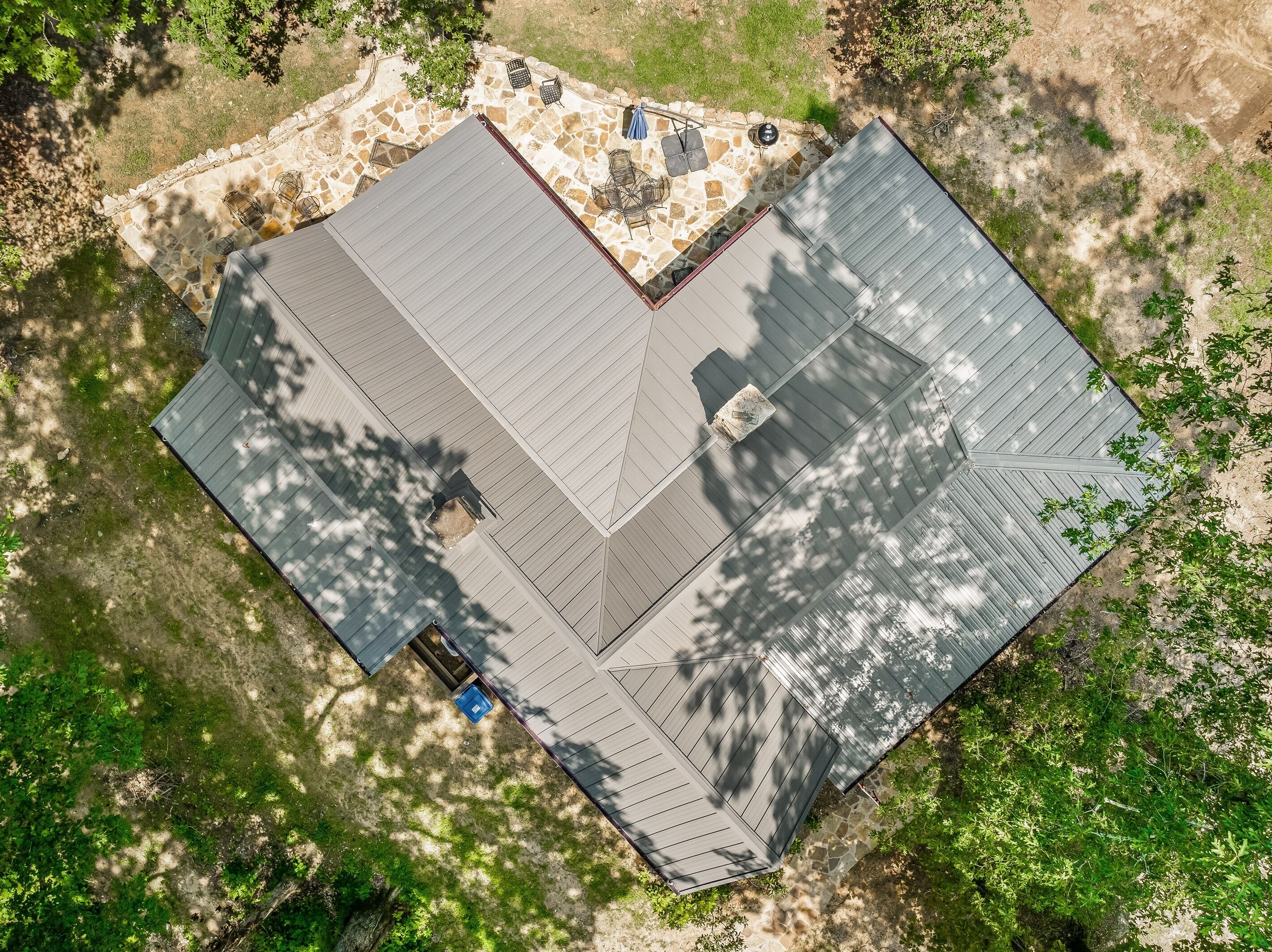 Vista aérea de una casa con un patio de piedra, una zona de estar cubierta al aire libre y un techo grande.