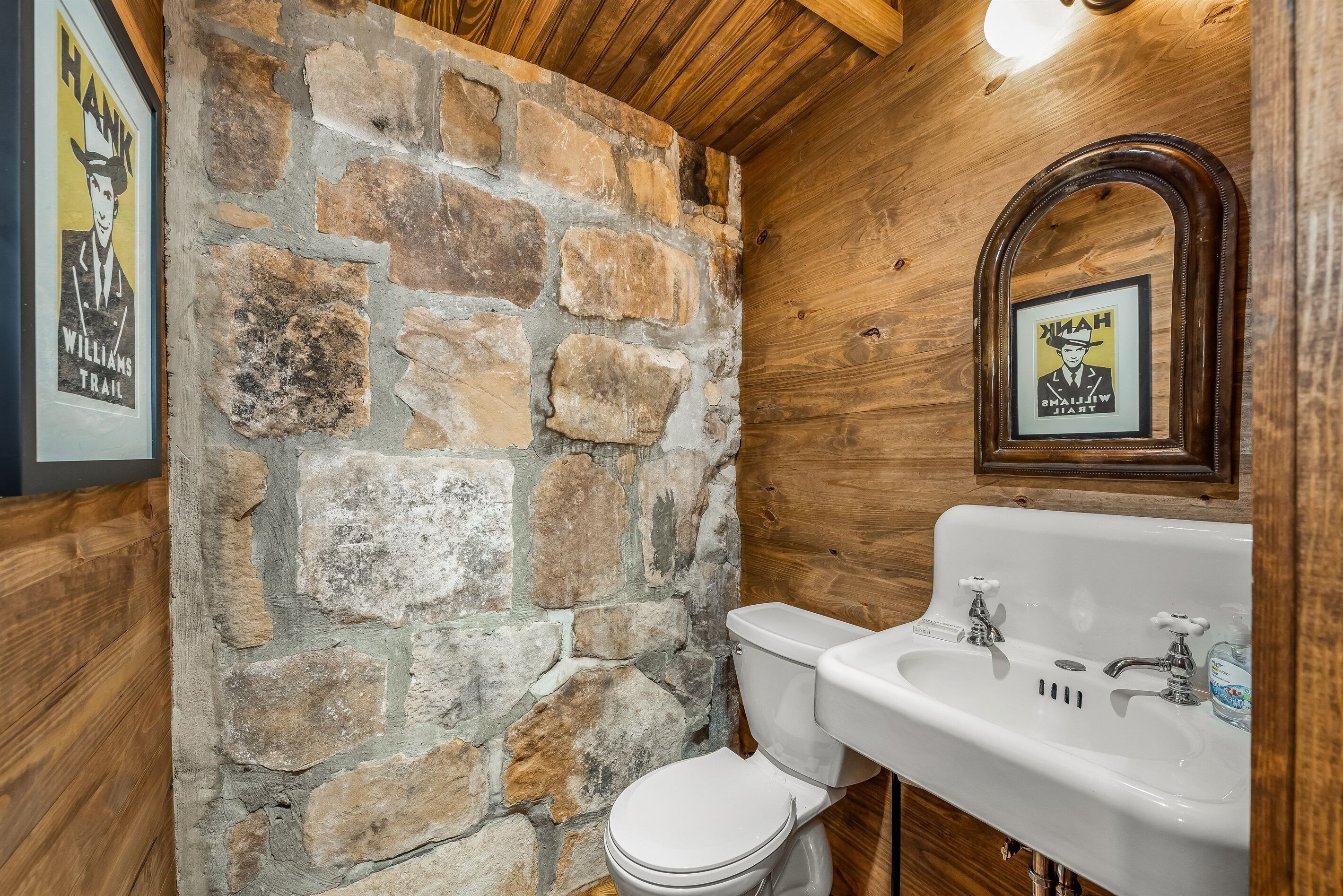 Un bagno con parete in pietra, soffitto in legno e lavabo bianco con due rubinetti.