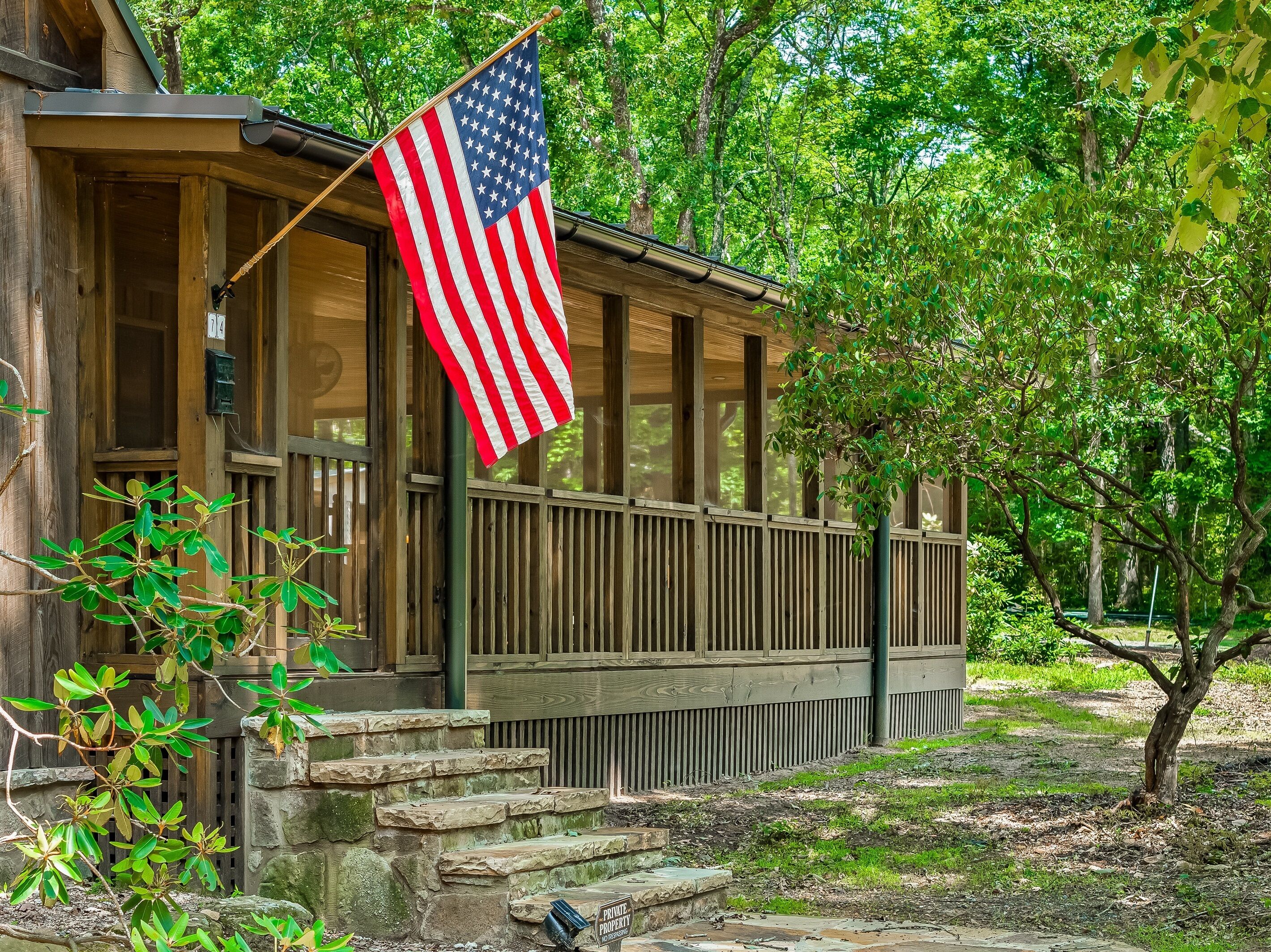 A wooden cabin with a porch, an American flag, and a private property sign.