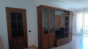 A room with a wooden cabinet with glass doors, a television, and a clock on the wall. - Accogliente Appartamento a 3 km da Sestri Levante con Parcheggio Privato (Casarza Ligure)