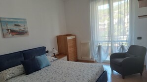 A bedroom with a bed, a chair, a dresser, a painting, and a window with curtains. - Accogliente Appartamento a 3 km da Sestri Levante con Parcheggio Privato (Casarza Ligure)