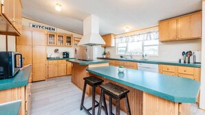 A kitchen with wooden cabinets, a central island with stools, a stainless steel refrigerator, and a coffee maker. - Set up for Crews- 10 beds, 5 bedrooms, 3 full bath (Byron)