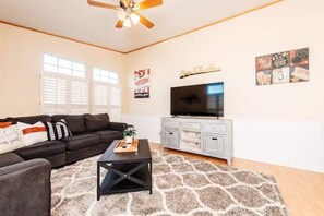A living room with a black sofa, a coffee table, a TV on a white cabinet, and a ceiling fan.