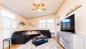 A living room with a sectional sofa, a coffee table, a TV, and a ceiling fan. - Set up for Crews- 10 beds, 5 bedrooms, 3 full bath (Byron)