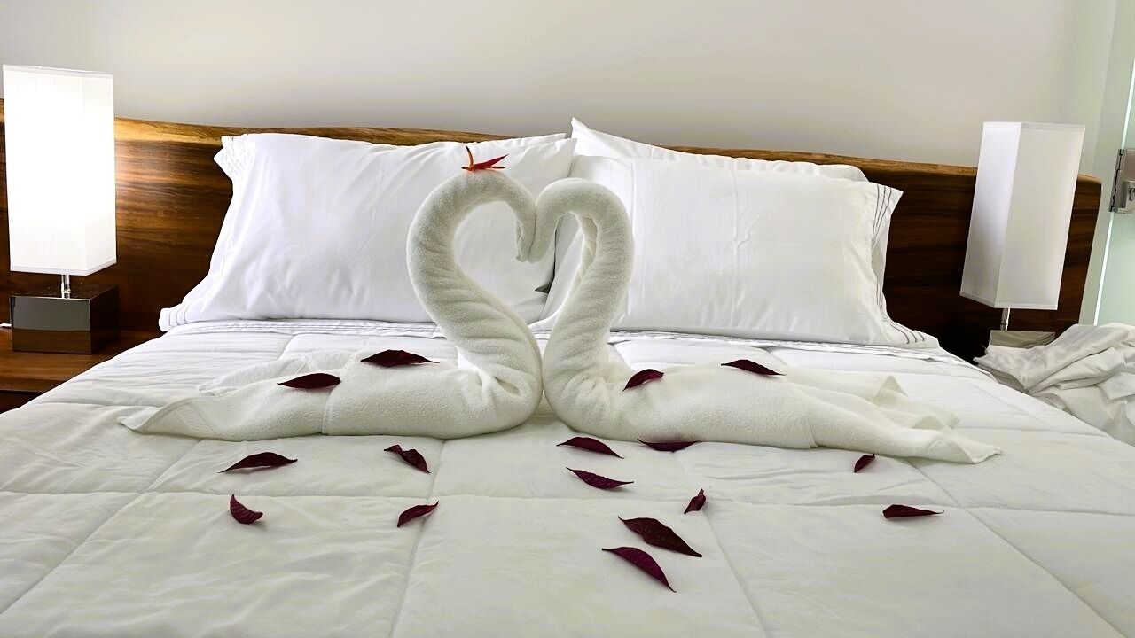 Une chambre d’hôtel avec un lit agrémenté d’une décoration en forme de cygne réalisée avec des serviettes et parsemée de pétales de rose.