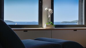 Una habitación con vista al mar a través de una ventana, una planta en maceta con flores blancas y un sofá azul oscuro.