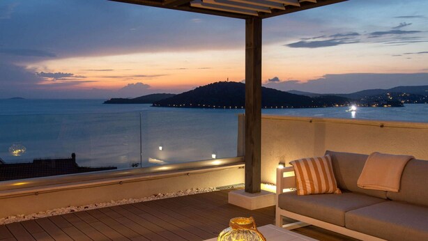 Un balcón con sofá y mesa, con vista a una masa de agua y una isla distante al atardecer.