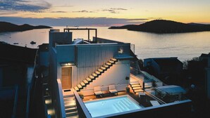 Una terraza moderna en la azotea con piscina, mobiliario exterior y una escalera que lleva al nivel superior.