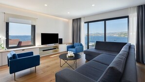 Una sala moderna con un televisor de pantalla plana grande, dos sillones azules, un sofá gris y una mesa de centro.