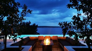 A poolside seating area with a fire feature, overlooking a body of water. - Villa Beatrice (Soho) (Starigrad)