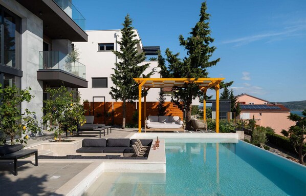 A modern outdoor pool area with a pergola, seating, and a view of surrounding buildings. - Villa Beatrice (Soho) (Starigrad)